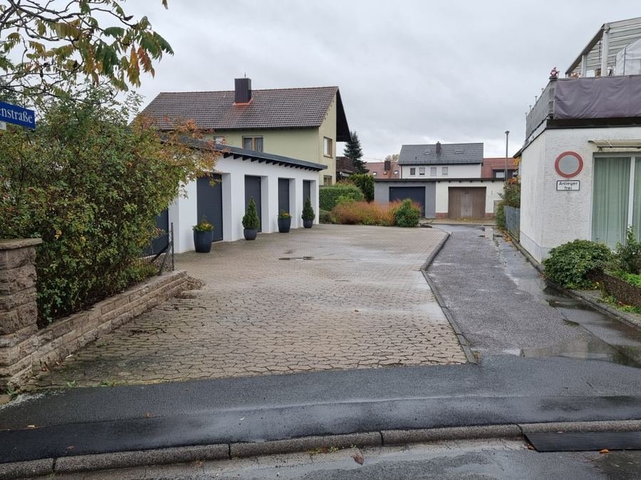 Blick von der Tulpenstraße mit Straßenschild auf die Zufahrt: links ein gepflasterter Hof mit Garagen, rechts ein schmaler asphaltierter Weg