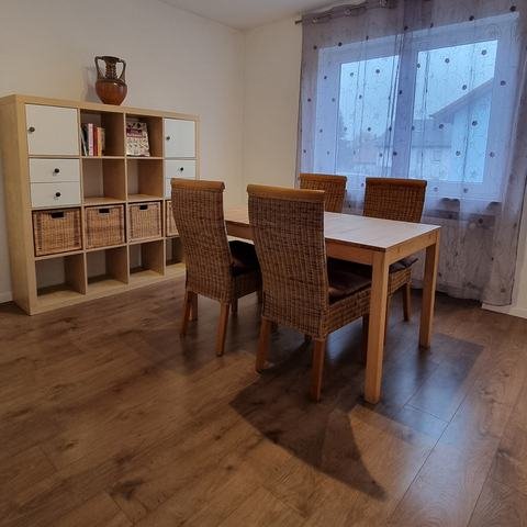 Esszimmer mit Holztisch, vier Korbstühlen, Regal mit Körben und Fenster mit Vorhängen