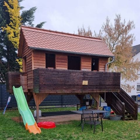 Garten mit hölzernem Spielhaus auf Stelzen, grüner Rutsche, Sandkasten und Gartentisch