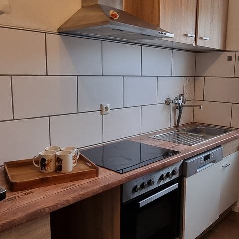 Küche mit Kaffeevollautomat, Tassen auf einem Holztablett, Ceranfeld, Backofen, Spülmaschine und Fenster