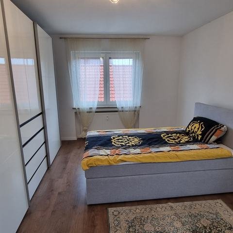 Schlafzimmer 2 mit hellgrauem Boxspringbett, großem weißem Schiebetürenschrank und Teppich