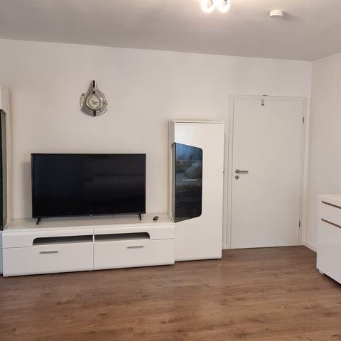 Wohnzimmer mit Fernseher auf weißem Lowboard, zwei Vitrinenschränken, Sideboard und einem bunten Bild an der Wand